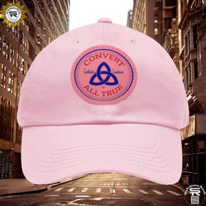 May include: Pink baseball cap with a brown leather patch featuring a blue Celtic knot and the text "CONVERT CATHOLIC TRADITION IS ALL TRUE".