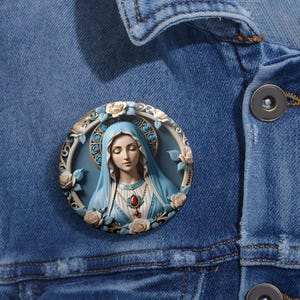 May include: A round button featuring a detailed illustration of the Virgin Mary in a blue robe with a crown of thorns and a red gemstone necklace. The image is surrounded by white roses and blue flowers.