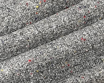 May include: Close-up of a gray tweed fabric with red, yellow, and blue flecks. The fabric has a textured, woven appearance.