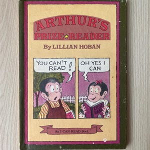 May include: A vintage children's book cover featuring a cartoon monkey reading a book titled "Little Bear". The cover is green, yellow, and red with the title "Arthur's Prize Reader" and the author "Lillian Hoban".