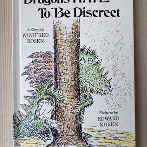 May include: A hardcover children's book titled "Dragons HATE To Be Discreet" with illustrations of a dragon and a person hiding behind a tree. The cover features text by Winifred Rosen and pictures by Edward Koren.