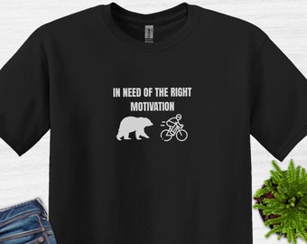 Könnte beinhalten: Schwarzes T-Shirt mit weißem Text "In need of the right motivation" und einer Grafik eines Bären, der vor einer Person auf einem Fahrrad davonläuft.