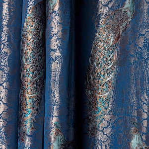 May include: A deep blue fabric curtain featuring a repeating jacquard pattern of peacocks in shades of teal, copper, and bronze. The textile displays a textured, metallic finish with intricate embroidery details depicting the birds in profile.