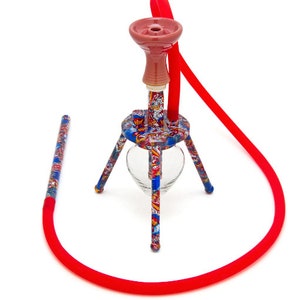 May include: A colorful, multi-colored hookah with a red hose and a red ceramic bowl. The hookah has a glass base and a tripod stand.
