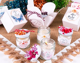 May include: Wedding favor candles in small glass jars with white lids and floral labels. The labels say "Alice & David" and have a floral design. The candles are surrounded by small boxes with floral designs and the text "Alice & David" on them.