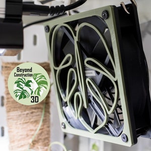 May include: A green 3D printed computer fan with a monstera leaf design. The fan is mounted on a white wall and has a black fan blade. The fan is labelled "Beyond Construction 3D".