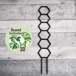 May include: Black metal plant trellis with six hexagonal openings. The trellis is designed to support climbing plants. The trellis is on a wooden background.