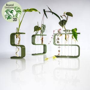 May include: Three green S-shaped plant stands with glass test tubes holding various plants. The stands are made of a smooth, matt green plastic. The text "Beyond Construction 3D" is visible in the top left corner of the image.