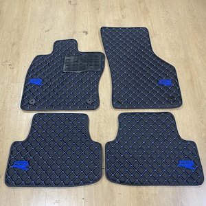 Könnte beinhalten: Ein Set aus vier schwarzen Autofußmatten mit blauem Rautensteppmuster. Jede Matte ist mit einem blauen R-Emblem versehen. Die Fahrermatte verfügt über eine schwarze, strukturierte Fersenauflage und zwei runde Befestigungslöcher.