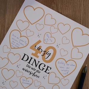 Puede incluir: Un papel blanco con contornos de corazón dorados y notas manuscritas, celebrando un 40 cumpleaños. Las palabras "40 Dinge" se muestran de forma destacada, con una flor rosa y un bolígrafo en el fondo.