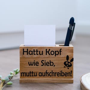 Könnte beinhalten: Schreibtisch-Organizer aus Holz mit dem Text "Hattu Kopf wie Sieb, muttu aufschreiben!" und einem Cartoon-Hasen. Er enthält eine weiße Karte und einen blauen Stift. Das Holz hat eine natürliche Oberfläche.