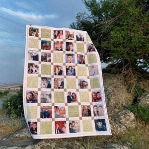 May include: A personalized photo quilt featuring a grid pattern with family photos. The quilt has a white border and green square accents. The photos are of various sizes and depict people of different ages. The quilt is displayed outdoors against a cloudy sky.