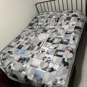 May include: A personalized quilt featuring a patchwork design of heart-shaped blocks. Each block displays a photograph, creating a collage of memories. The quilt is primarily gray and white, with a dark gray border. The bed frame is black.