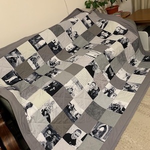 May include: A gray patchwork quilt featuring a variety of black and white photographs. The quilt is made of square patches in shades of gray and white, with a solid gray border. The photographs appear to be of people and various scenes.