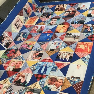 Op de afbeelding: Een handgemaakte quilt met een patchwork ontwerp van driehoekige stukken stof. Elke driehoek toont een andere foto. De quilt is omrand met een effen blauwe stof. De quilt ligt op een grijze bank.