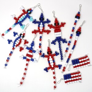 May include: A collection of red, white, and blue beaded lizard and flag charms. The charms are made with small, round beads and feature a variety of designs, including a lizard with a long tail, a flag with stars and stripes, and a simple flag.