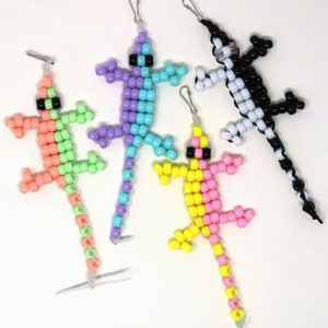 May include: Four beaded lizard keychains in different color combinations: pink and yellow, light green and pink, purple and blue, and black and white.