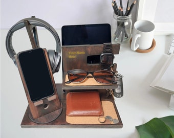 May include: A dark brown wooden desk organizer with compartments for a phone, headphones, tablet, watch, and glasses. It also has a small cork-lined tray for a wallet, keys, and coins. The text "Your Name Here" is visible.