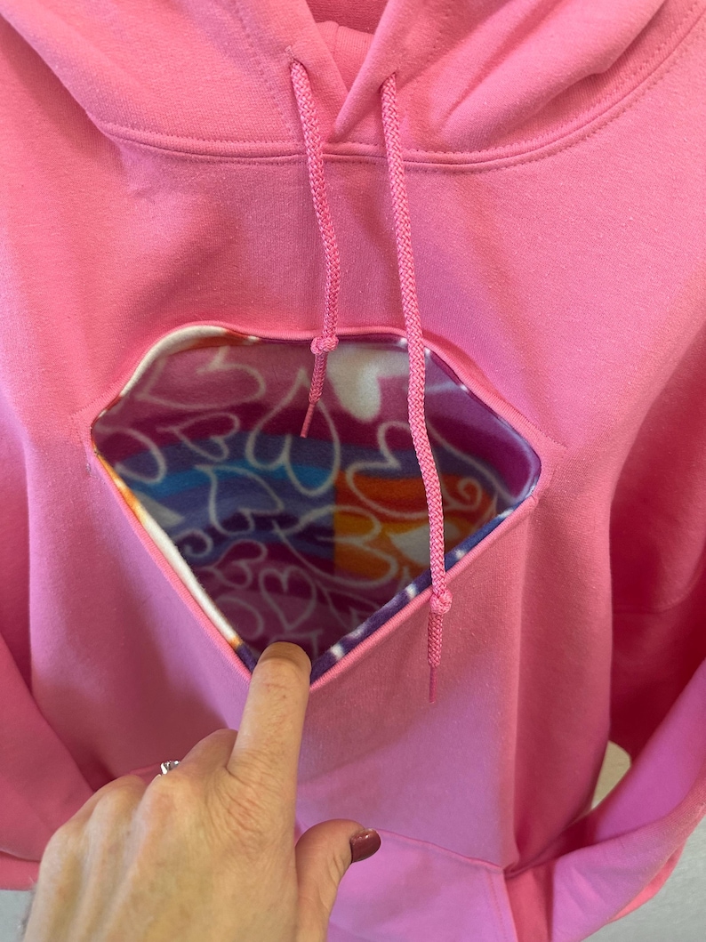 May include: Pink hoodie with a heart-shaped opening revealing a colourful fleece lining.