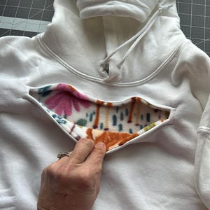 May include: White hooded sweatshirt with a floral and brown patterned fleece lining visible through a cut-out in the front.
