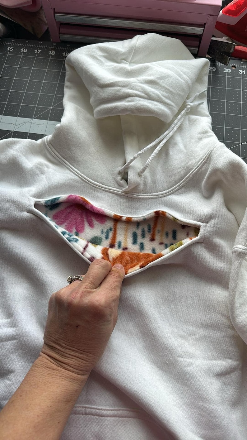 May include: White hooded sweatshirt with a floral and brown patterned fleece lining visible through a cut-out in the front.
