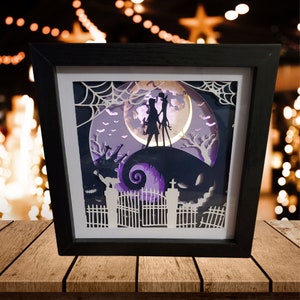 May include: A black framed 3D paper art shadow box with a purple and white scene of Jack Skellington and Sally from the Nightmare Before Christmas movie. The scene is lit from behind with a white light.