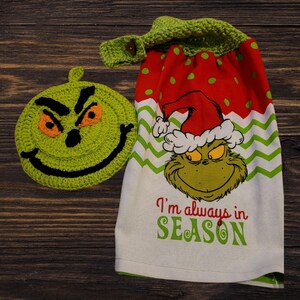 Könnte beinhalten: Ein grüner, gehäkelter Grinch-Gesichts-Geschirrtuch mit einem roten und weißen Tupfen- und grün-gewellten Muster-Küchenhandtuch mit dem Grinch, der einen Weihnachtsmann-Hut trägt und den Text "I'm always in SEASON".