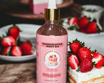 Op de afbeelding: Een roze en witte fles handgemaakte aardbeien-shortcake-lichaams olie. De fles heeft een gouden dop en een druppelaar. Het etiket zegt "Handcrafted Body Oil" en "Strawberry Shortcake". Het zegt ook "Moisturize & Radiate Delicious" en "Bloom2Bliss.com".