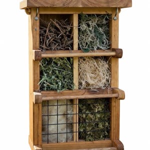 May include: A wooden insect hotel with six compartments filled with various natural materials. The compartments are arranged in a grid, and the hotel has a roof and decorative wooden handles. The materials include twigs, dried grasses, and moss.