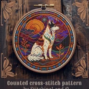 Peut inclure: Mod&egrave;le de point de croix compt&eacute; repr&eacute;sentant un loup blanc avec des marques brunes et noires, assis dans un paysage color&eacute; avec un coucher de soleil et des montagnes. Le motif est dans un cercle de broderie rond.