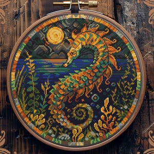 Puede incluir: Patrón de punto de cruz contado de un caballito de mar con una luna y estrellas en el fondo. El caballito de mar es naranja, amarillo y verde. El fondo es azul, verde y negro. El patrón está en un aro de bordado de madera redondo.