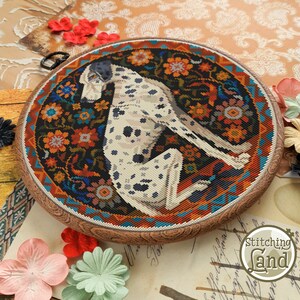 May include: A circular embroidery hoop with a colorful floral design and a white and black Dalmatian dog sitting in the center. The hoop is made of wood and has a brown finish.