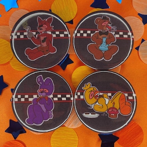 May include: Set of four round buttons featuring cartoon characters in various poses. Each button has a dark brown background with a white and black checkered stripe. The characters are in red, brown, purple, and yellow.