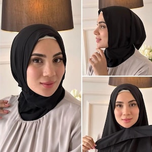 May include: A solid black hijab made of a smooth, opaque fabric that covers the head and neck. The head covering is styled with a clean, draped fit, featuring a simple wrap design that frames the face and secures neatly around the chin and shoulders.
