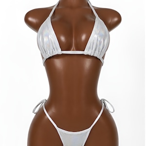 May include: A two-piece bikini set in a metallic silver, iridescent fabric. The top features triangular cups with gathered detailing and thin halter straps. The matching bottom has a high-cut leg design with thin side ties for an adjustable fit.