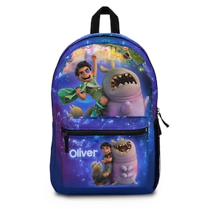 Puede incluir: Mochila azul con un diseño de dibujos animados colorido que muestra a un niño y un monstruo. La mochila tiene un asa negra y un bolsillo frontal con el nombre "Oliver" impreso en blanco. El fondo es un cielo estrellado.