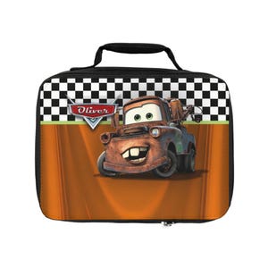 Puede incluir: Una lonchera rectangular con el personaje Mate de la pel&iacute;cula Cars. La bolsa tiene un asa y cremallera negras, con un patr&oacute;n de cuadros en la parte superior. El fondo es naranja con una franja verde.