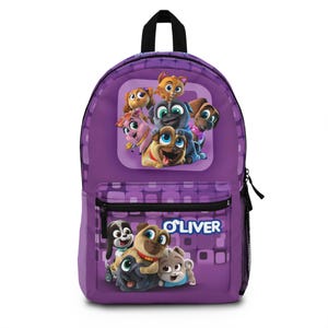 Puede incluir: Mochila morada con cachorros de dibujos animados y el nombre "O'LIver". Tiene un bolsillo frontal, un bolsillo lateral y un asa negra. El diseño principal presenta un grupo de cachorros animados de varios colores.