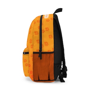 May include: An orange backpack with a black back and straps. The backpack features a pattern of orange paw prints and a black zipper. A mesh pocket is on the side. The word "DOG" is printed on the top.