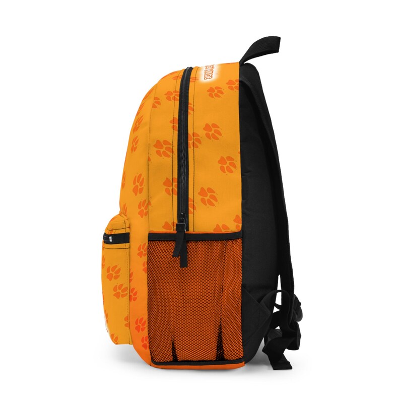 May include: An orange backpack with a black back and straps. The backpack features a pattern of orange paw prints and a black zipper. A mesh pocket is on the side. The word "DOG" is printed on the top.