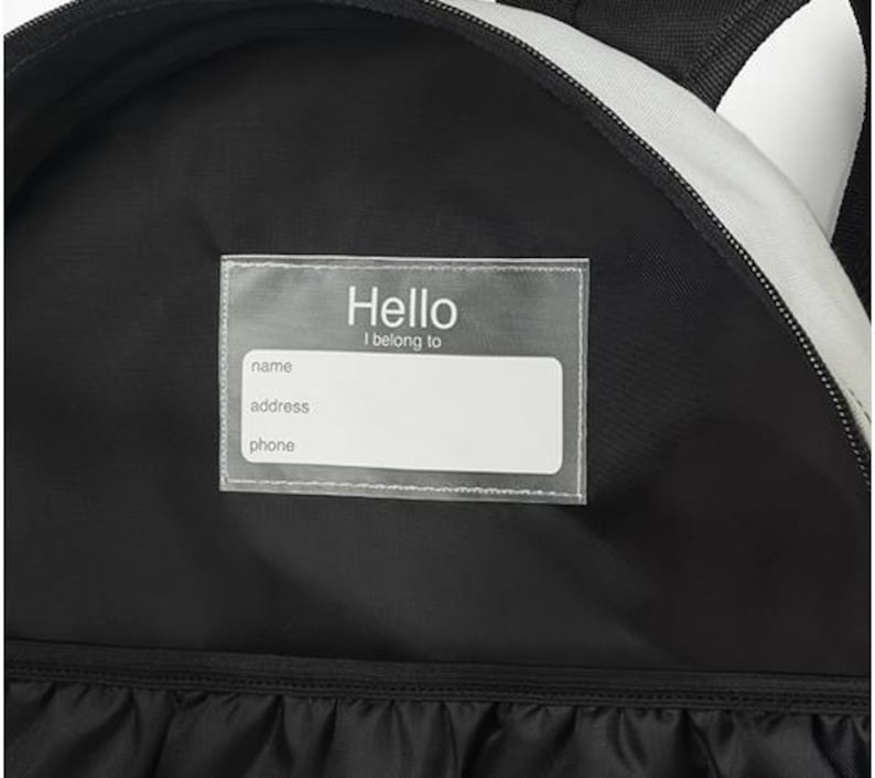 May include: Black backpack interior with a clear label that reads "Hello I belong to" above blank fields for name, address, and phone. The backpack has a black and white striped design on the exterior.