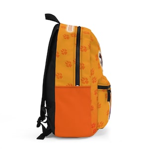 May include: Orange backpack with a black back and straps. The front of the backpack has a paw print pattern and a solid orange pocket. The top of the backpack has the word "Cody" in white text.