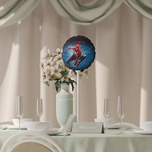 May include: A table setting with a light green tablecloth, white dishes, and champagne flutes. A vase of white flowers and a Spider-Man balloon centerpiece with the name "Oliver" are featured. A "Reserved" sign is on the table.