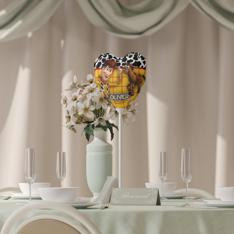 K&ouml;nnte beinhalten: Ein herzf&ouml;rmiger Ballon mit einem Cowboy-Cartoon-Design und dem Namen "Oliver". Der Ballon ist Teil einer Tischdekoration mit wei&szlig;en Blumen in einer Vase, Sektgl&auml;sern und einem "Reserviert"-Schild.
