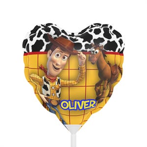 K&ouml;nnte beinhalten: Herzf&ouml;rmiger Ballon mit Woody aus Toy Story, mit einem schwarz-wei&szlig;en Kuhdruck oben. Der Ballon hat einen gelben Hintergrund mit einem Rastermuster und dem Namen "OLIVER" in Blau. Ein braunes Pferd ist ebenfalls abgebildet.