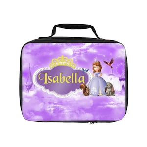Puede incluir: Una bolsa de almuerzo morada con un diseño de princesa y el nombre "Isabella" en letras doradas. La bolsa tiene un asa y cremallera negras, con imágenes de una princesa, una ardilla, un conejo y pájaros.