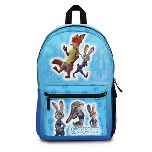 May include: A light blue backpack featuring characters from the movie Zootopia. The backpack has a large main compartment, a front pocket, and side mesh pocket. The name "SOPHIA" is printed on the front. The backpack has a black handle and straps.