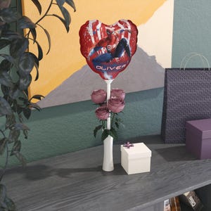 May include: A heart-shaped red balloon featuring Spider-Man, with the name "OLIVER" printed on it, is held above a bouquet of pink roses in a white vase. A small gift box with a purple ribbon sits nearby.