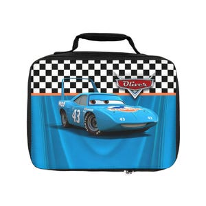 Puede incluir: Una bolsa de almuerzo azul con un coche de carreras de dibujos animados, el n&uacute;mero 43. La bolsa tiene un asa negra y un patr&oacute;n de cuadros blanco y negro en la parte superior. El nombre "Oliver" se muestra en la bolsa.
