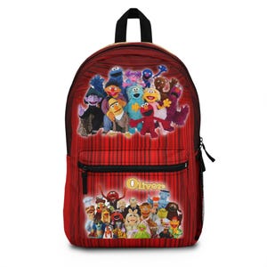 May include: Red backpack featuring a vibrant collage of Sesame Street characters against a backdrop of red curtains. The backpack has a black handle, a front pocket with a zipper, and the name "Oliver" in gold lettering.